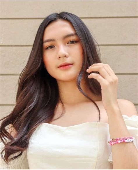 A Woman With Long Hair Wearing A White Top And Pink Bracelets On Her Wrist