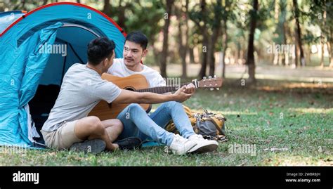 LGBTQIA Gay Couple Camping Together In Woods For Holidays And Relax On Guitar Together Stock