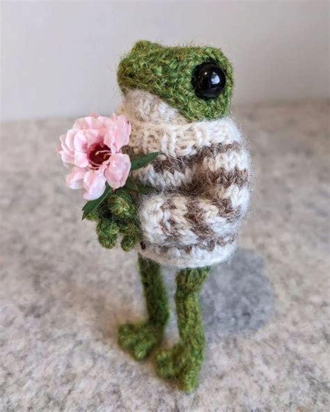 A Small Stuffed Frog Holding A Pink Flower