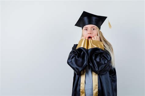 Fille blonde mettant la main près de la bouche ouvrant la bouche en robe de graduation et