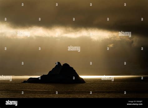 Sunlight Shining Through A Hole In The Clouds Silhouette Of An Iceberg