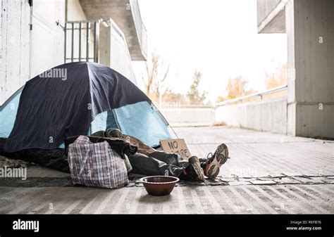 Legs And Feet Of Homeless Beggar Man Lying On The Ground In City