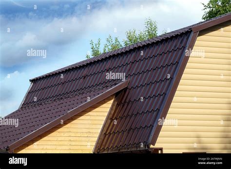 Brown metal roof of rural house covered with yellow siding over blue ...