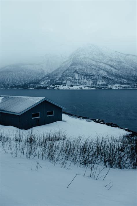 A small cabin in the snow near a lake · Free Stock Photo