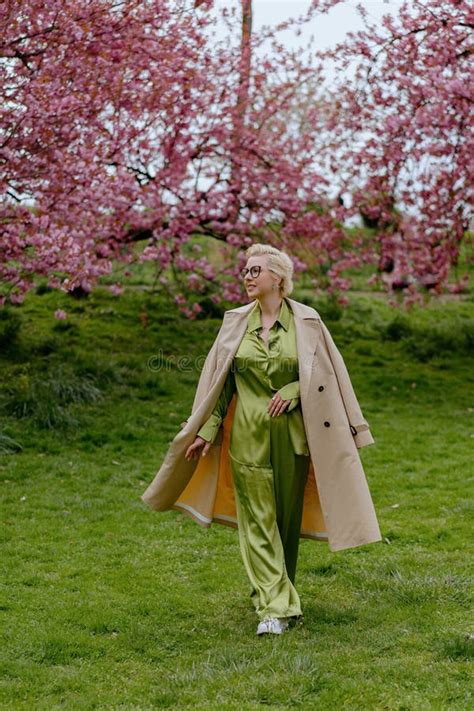 A Blonde Woman In Green Outfit Poses Surrounded By Cherry Blossoms Outdoors Stock Image Image