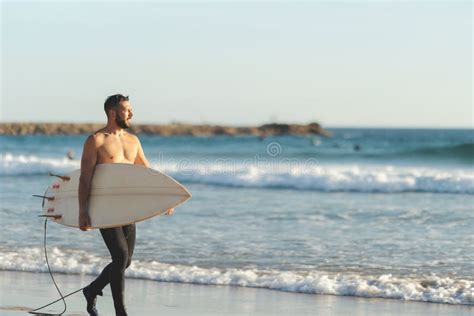 A Man With A Naked Torso Walking On The Beach Holding A Surfboard View From The Back Stock