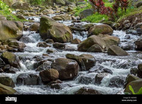 A Narrow River Stream Flowing Rapidly Over Large Rocks And Boulders