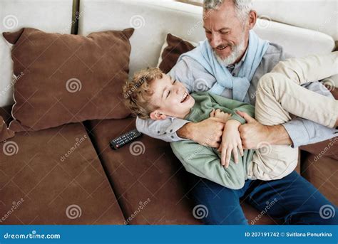 Grandson Embracing Grandpa Sitting On Couch Reading Book Royalty Free