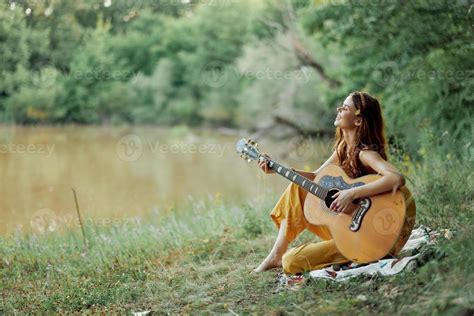 Hippie woman playing guitar smiling and singing songs in nature sitting ...