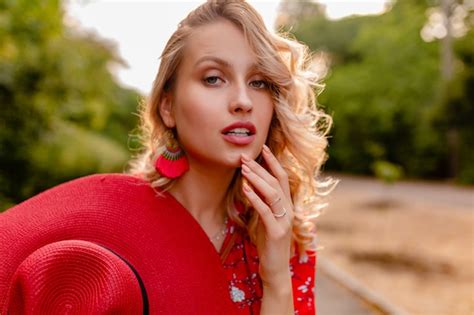 Attraktive stilvolle blonde lächelnde Frau in strohrotem Hut und Bluse Sommermode Outfit