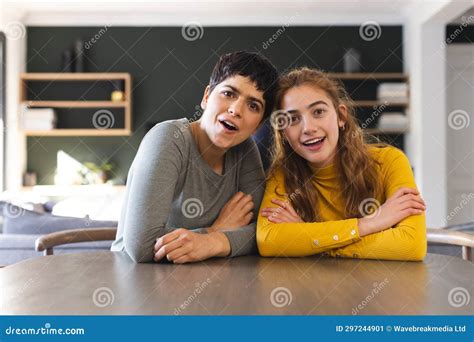 Happy Surprised Biracial Lesbian Couple Sitting At Dining Table Having Video Call At Home