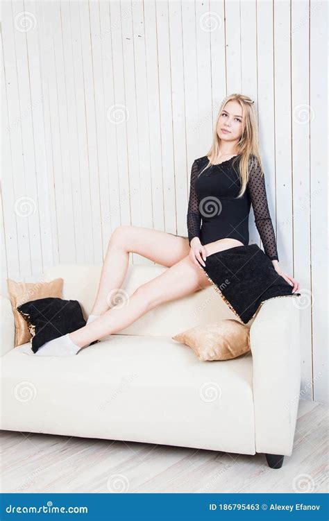 Girl In Black Underwear And Long Blonde Hair Poses Against A White Wall