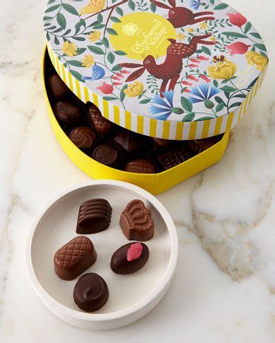 A Yellow Box Filled With Chocolates Next To A White Plate On A Marble