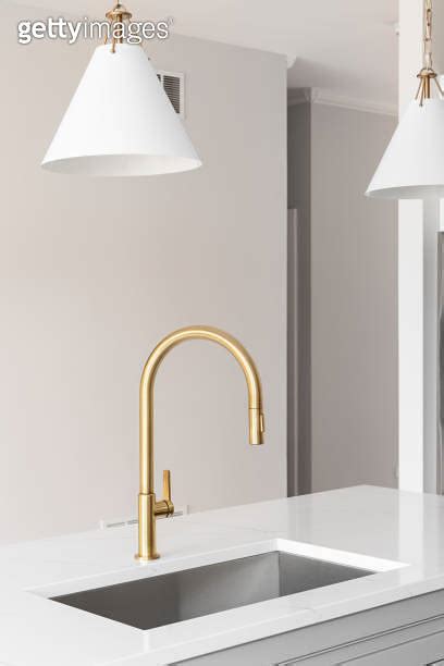 A Gold Kitchen Faucet Detail With White And Gold Lights Hanging Above