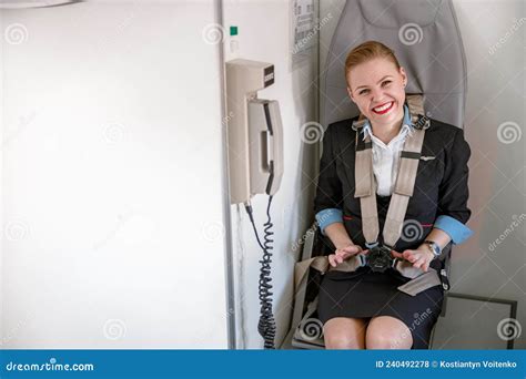 Cheerful Female Flight Attendant Sitting In Chair In Airplane Stock