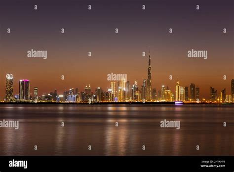 Dubai Business Bay skyline at night with colorful illuminated buildings and calm Dubai Creek ...