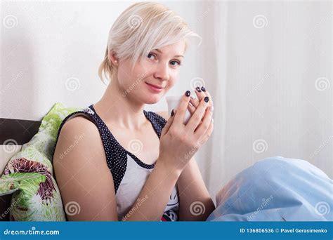 Jeune Belle Blonde Aux Cheveux Courts Assise Sur Son Lit Et Tenant Une Boisson Chaude Photo