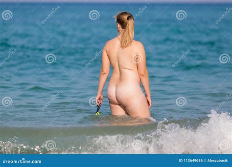 Naked Woman Enters The Sea With Swimming Glasses In Hand Stock Photo