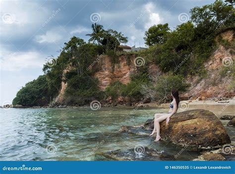 Giovane Bella Donna Sexy In Bikini Che Si Siede Sulle Rocce Alla Spiaggia Immagine Stock