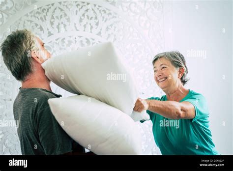 Old And Youthful People Mature Retired Man And Woman Play At Home At War Pillow In The Bedroom