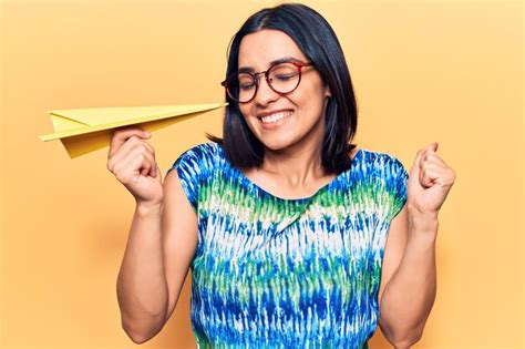 Jovem linda mulher latina segurando avião de papel gritando orgulhoso comemorando a vitória e