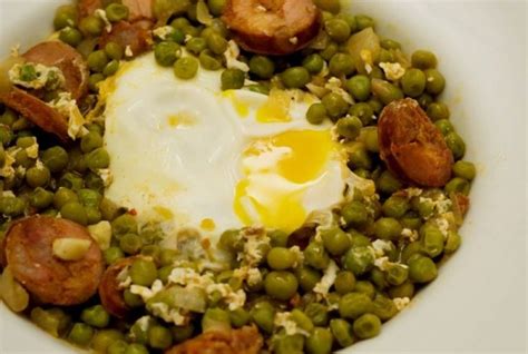 A White Bowl Filled With Peas Sausages And An Egg On Top Of It