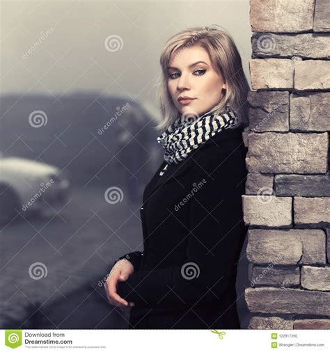 Fashion Blond Woman In Black Coat Leaning On Wall In City Street Stock