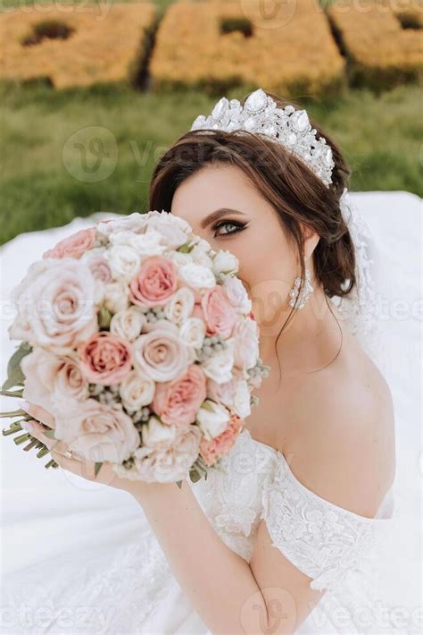 brunette la mariée dans hors de l épaule dentelle blanc robe et tiare posant avec une bouquet de