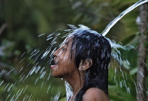 A Woman Is Spraying Water On Her Face And Head With Trees In The Back