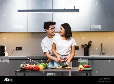 Asian Couple Cooking Together Making Salad Hugging In Modern Kitchen