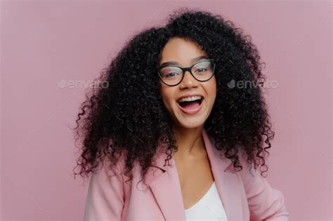 Portrait Of Pleased Young Curly Haired Woman Feels Overemotive Keeps