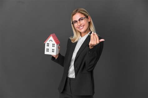 Fille blonde uruguayenne tenant un jouet de maison isolé sur fond noir invitant à venir avec la