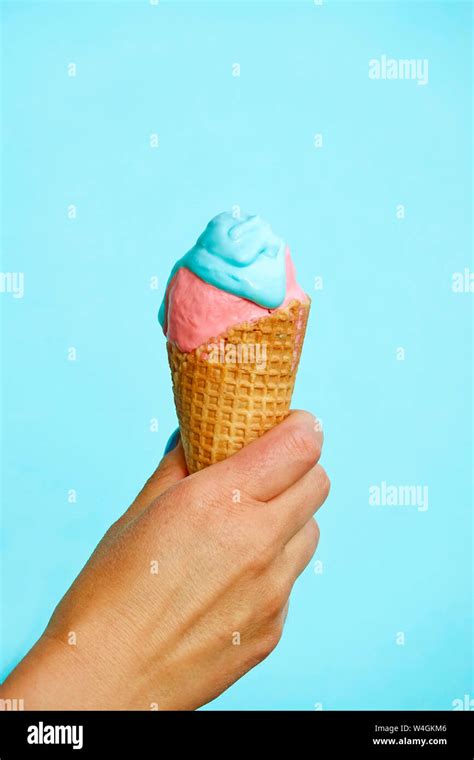 Womans Hand Holding Ice Cream Cone In Front Of Blue Background Stock