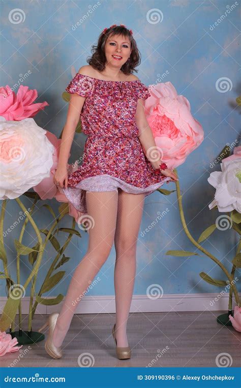 Long Legged Brunette Girl In White Fishnet Stockings And Minidress Posing At The Flowers Stock