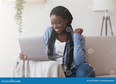 Young Black Woman Celebrating Success with Laptop on Sofa at Home ...