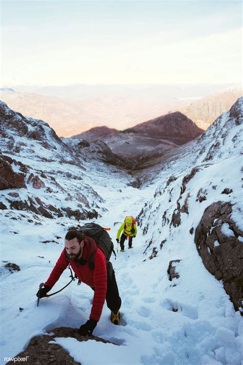 Two People Climbing Up The Side Of A Snow Covered Mountain