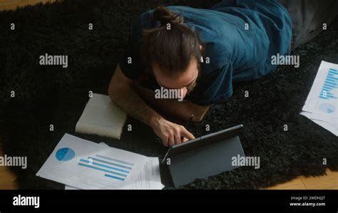 High agle shot of young adult student with long hair, wearing wireless headphones, lying on the ...