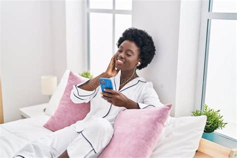 Young African American Woman Listening To Music Sitting On Bed At