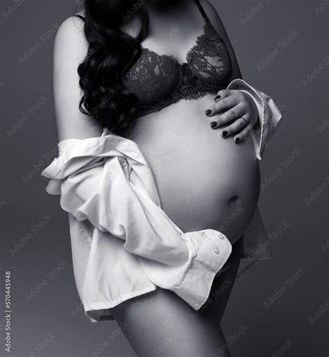 Expecting Mother In Black Lingerie Touching And Showing Her Pregnant Belly Against Light Gray