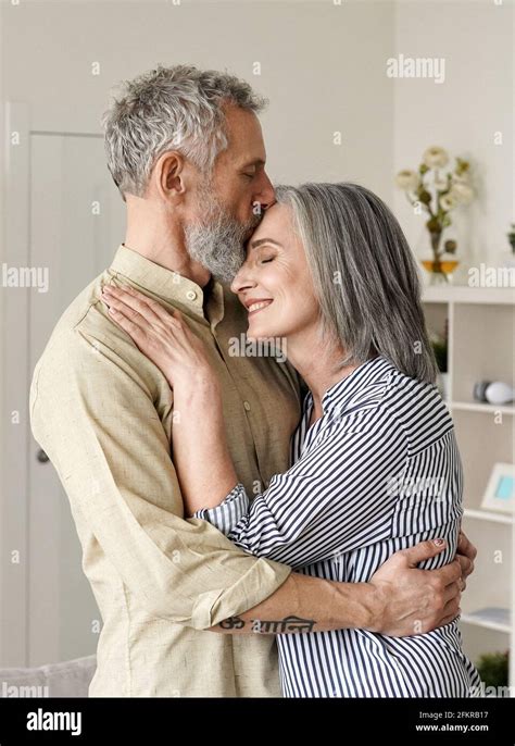 Smiling Mid Age Older Couple Hugging And Kissing Standing At Home Stock