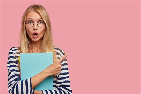 Étudiante blonde horrifiée posant contre le mur rose Photo Gratuite