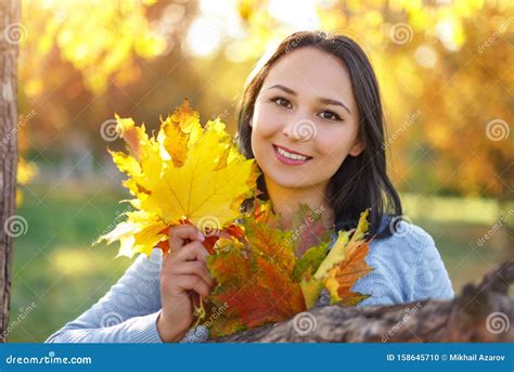 Portrait Of Smiling Young Woman With Autumn Leafs In Front Of Foliage