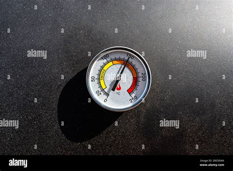 A round thermometer showing 150 degrees Celsius placed on a charcoal ...