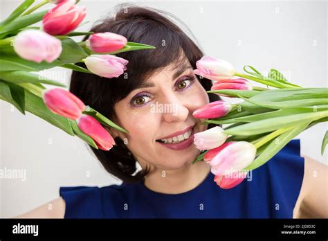 Portrait Of An Adult Brunette Covering Her Face With Two Bouquets Of Tulips On A White