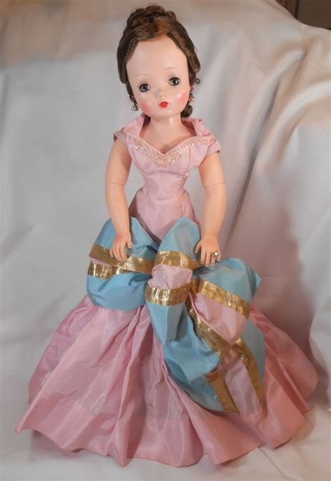 A Doll Sitting On Top Of A Blue And Pink Dress With Gold Trimmings