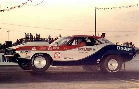 An Old Race Car Driving Down The Street In Front Of A Large Group Of People