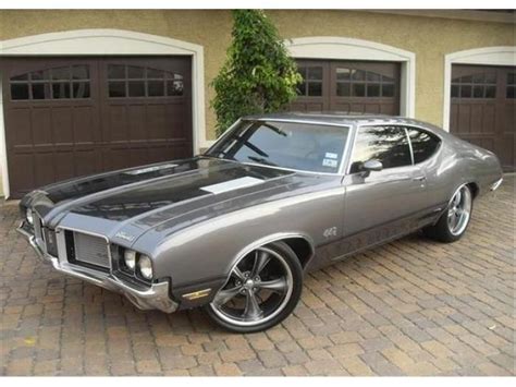 A Gray Muscle Car Parked In Front Of Two Brown Garage Doors On A Brick