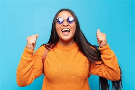 Mujer latina joven que parece extremadamente feliz y sorprendida celebrando el éxito gritando