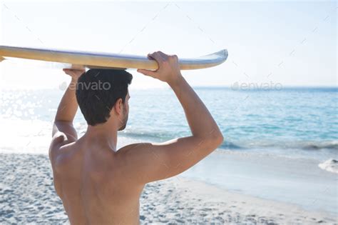 Rear View Of Shirtless Man Carrying Surfboard At Beach Stock Photo By