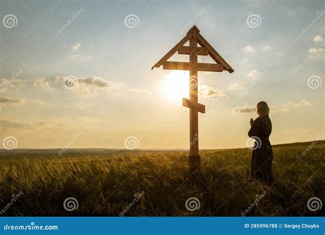 Woman Prays In Front Of A Christian Cross At Sunset Stock Photo